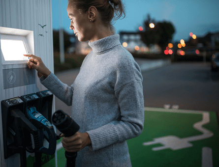 Woman charging her electric car at a public EV station — highlighting eco-friendly driving.