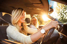 Two smiling women in a car during golden hour, with the driver enjoying the ride.